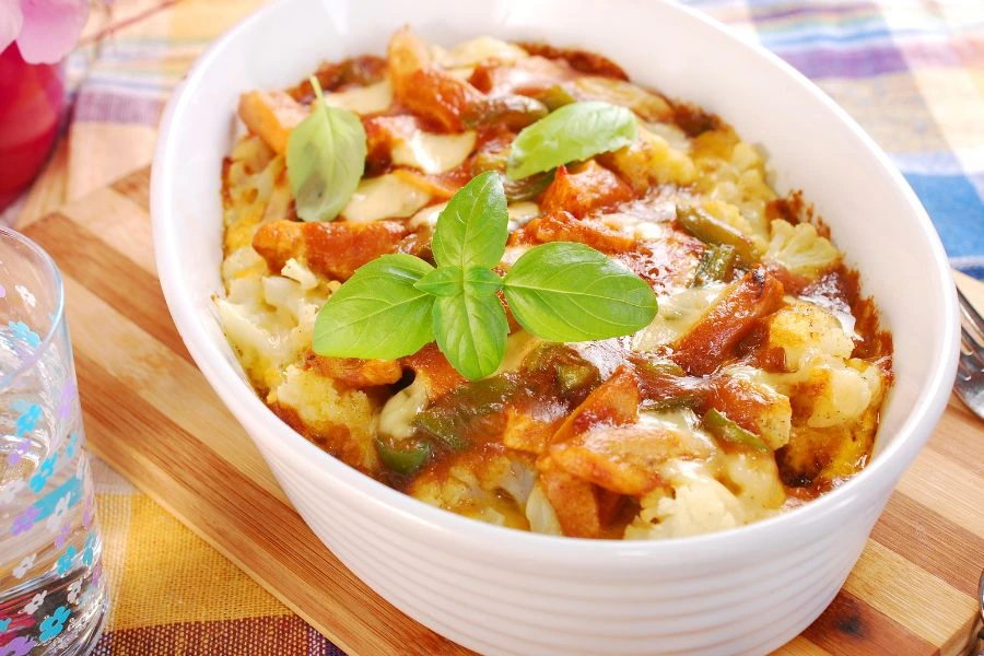 Prato branco com pedaços de Couve-Flor com Frango ao Curry, acompanhado de folhas verdes frescas. Refeição apresentada sobre uma mesa de madeira clara, ideal para quem busca uma opção saborosa e saudável.