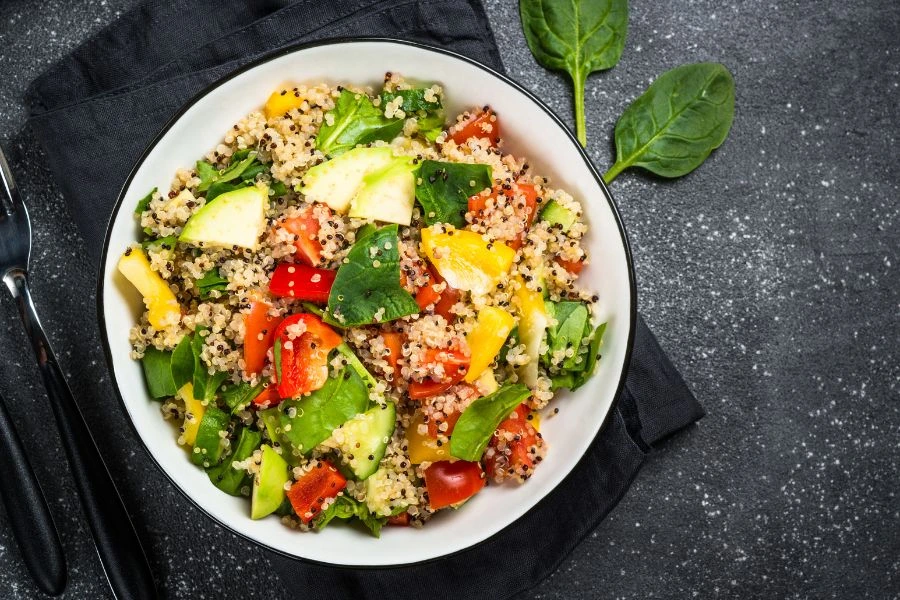 Salada saudável de Quinoa com Legumes Salteados em um prato branco sobre fundo preto. Receita equilibrada ideal para uma dieta nutritiva.